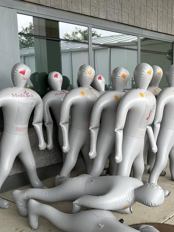 A group of training mannequins used for mass casualty training, some standing and one lying on the ground, placed outside a building.